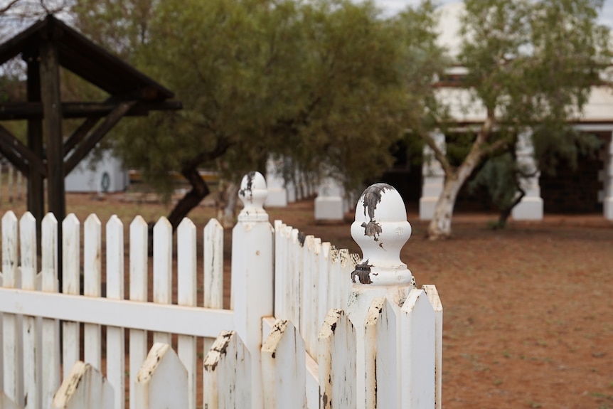 A ageing wooden picket fence in front of a white 19th century building