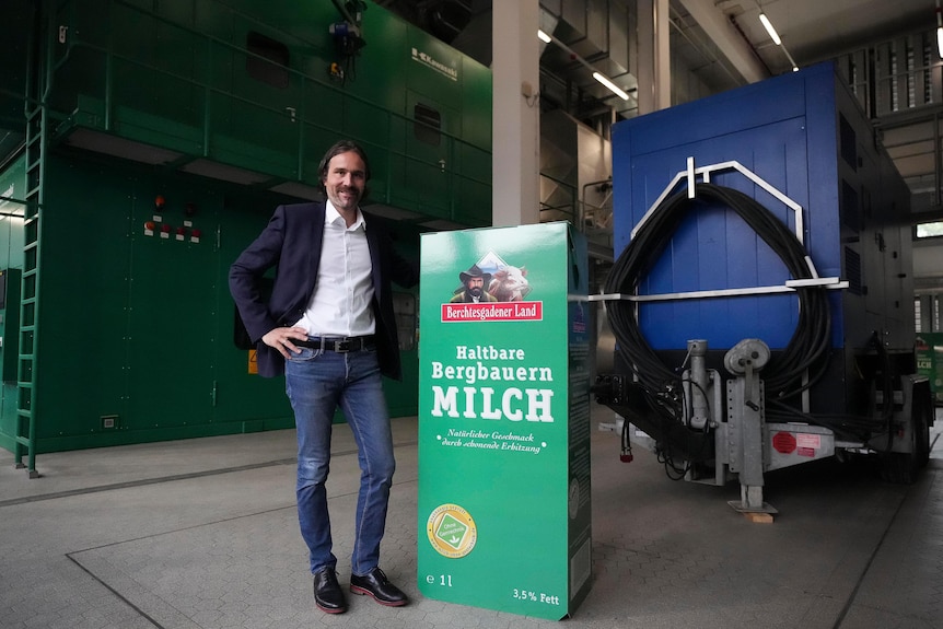 A man poses next to a board advertising milk in front of a turbine generator