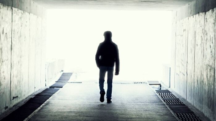 Man walking towards the light at the end of a dark tunnel.