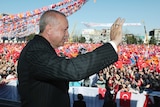 Erdogan waves to a large crowd of supporters waving flags.