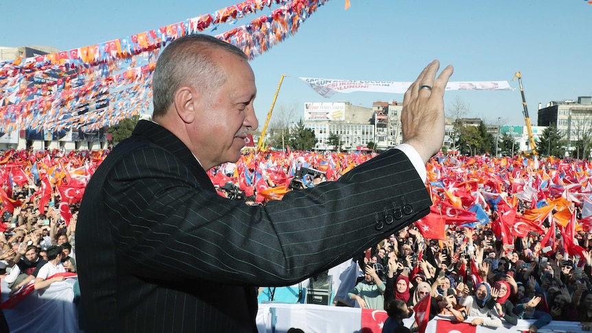 Erdogan waves to a large crowd of supporters waving flags.