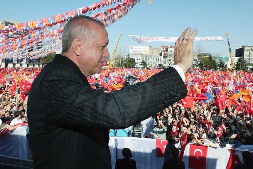 Erdogan waves to a large crowd of supporters waving flags.