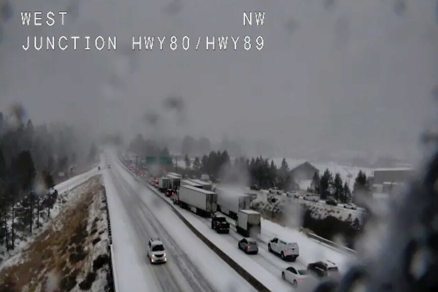 A road traffic camera shows backed-up cars and trucks on a snow-covered road in California.