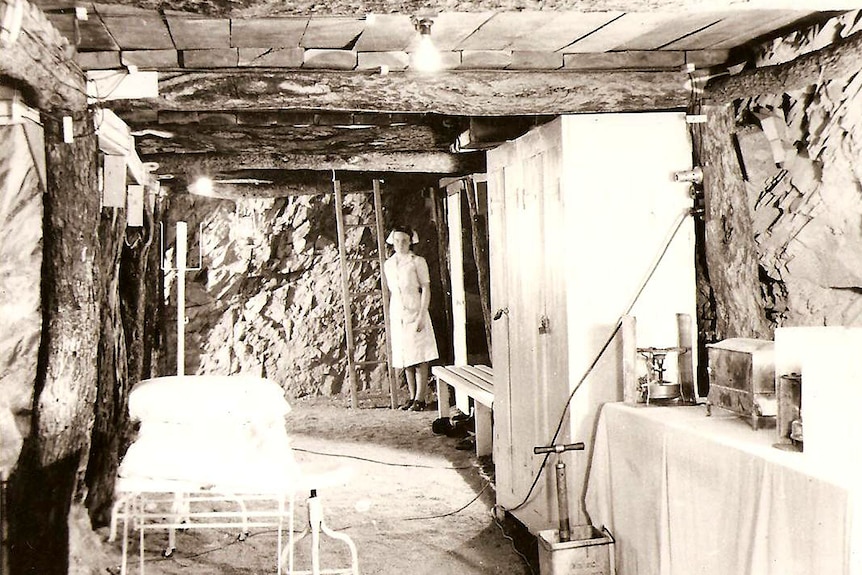A black and white photo of an underground hospital with dirt walls and hospital beds