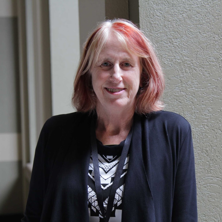 A woman with red hair standing by a railing and smiling at the camera.