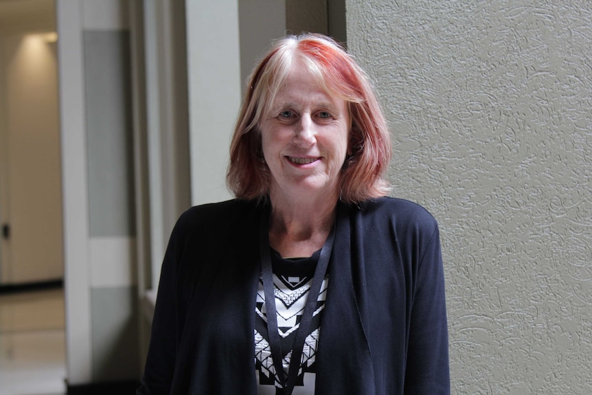 A woman with red hair standing by a railing and smiling at the camera.