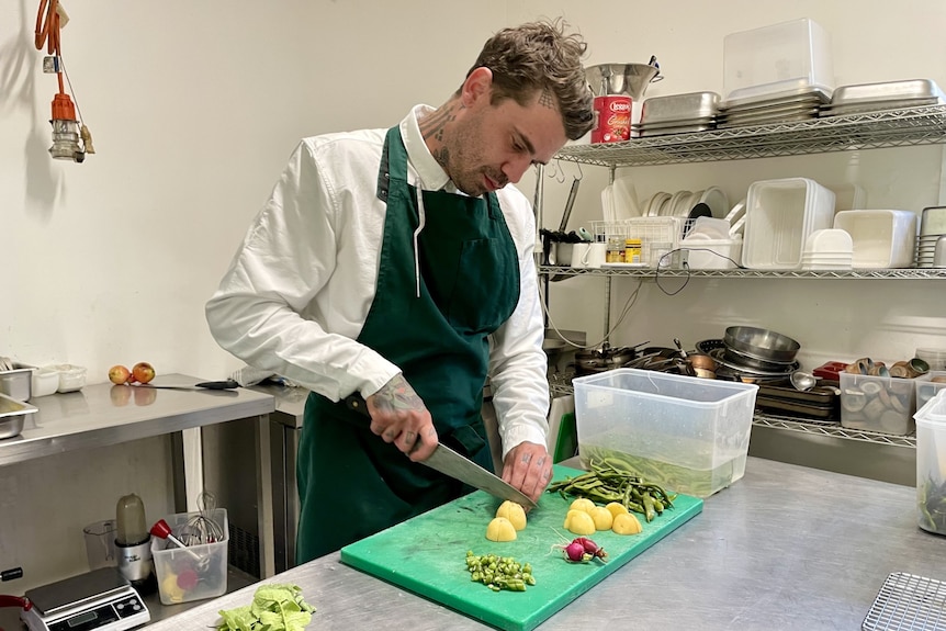 A man in a chef's apron chops up vegetables in a commercial kitchen.