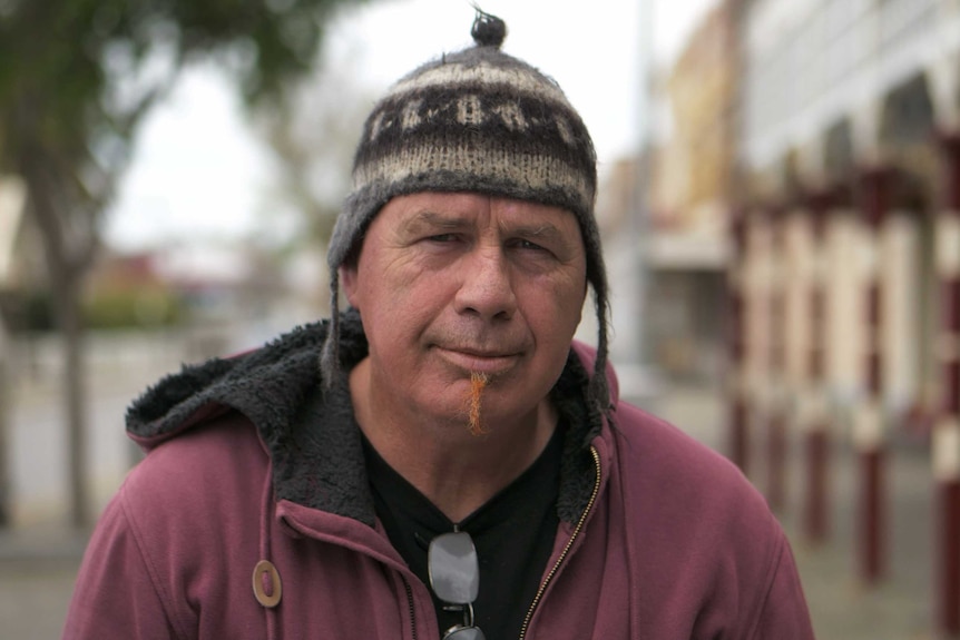 A man with a hat and coat on standing in a street.