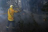 A firefighter uses a hose to spray water over a fence.