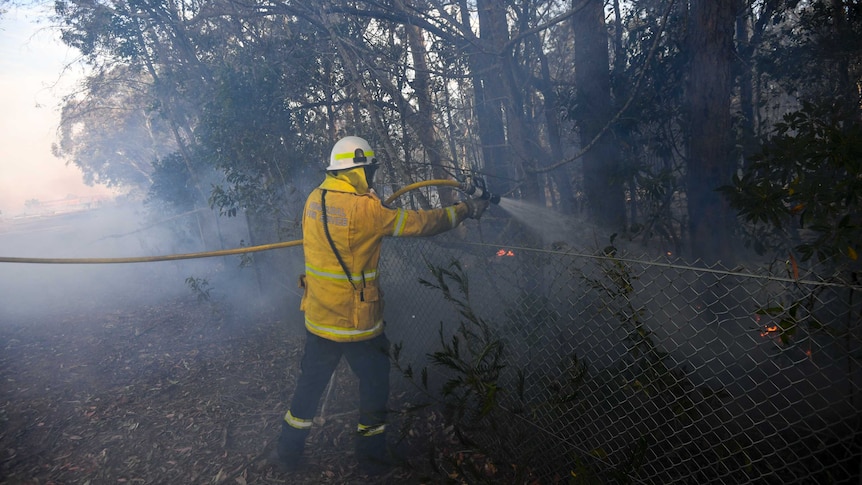 A firefighter uses a hose to spray water over a fence.