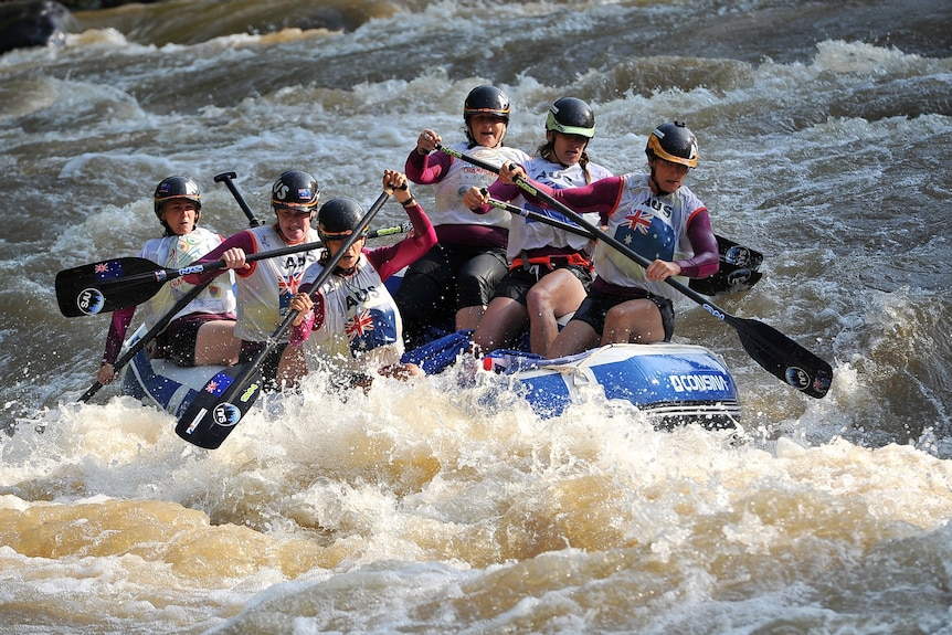 A rafting boat full of women goes over a rapid.