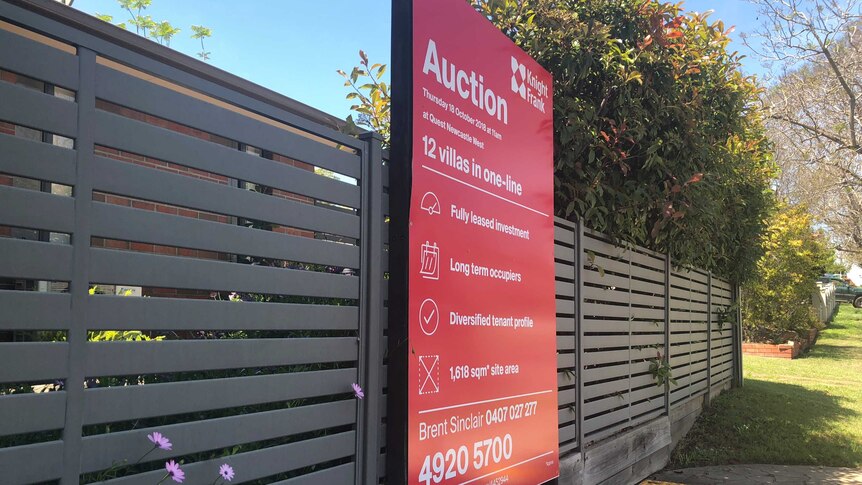 An auction sign on a fence outside a row of villas.