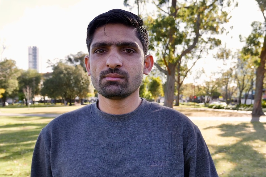 A man with a moustache and beard stands in a park