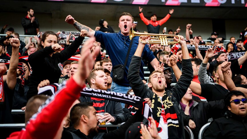 A man in a navy jumper stands out among a crowd of red and black.