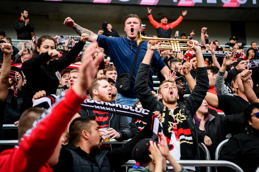 A man in a navy jumper stands out among a crowd of red and black.