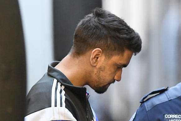 A handcuffed young man wearing a black jumper walks with his head down.