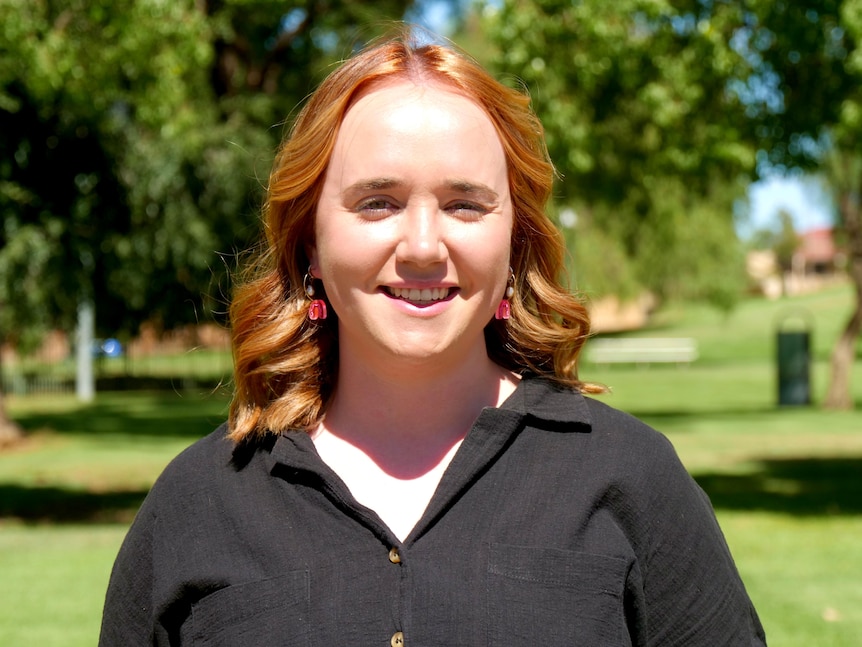 A red headed white woman wearing a black shirt smiling in a park. 