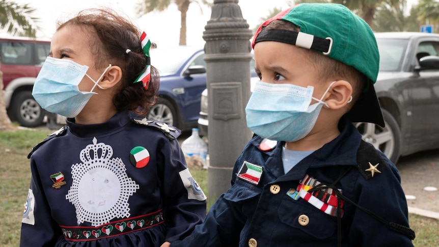 Two toddlers, one girl and one boy, wear surgical masks on the street.