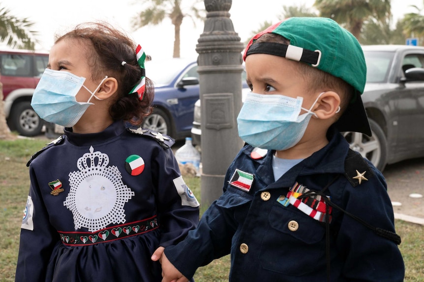 Two toddlers, one girl and one boy, wear surgical masks on the street.