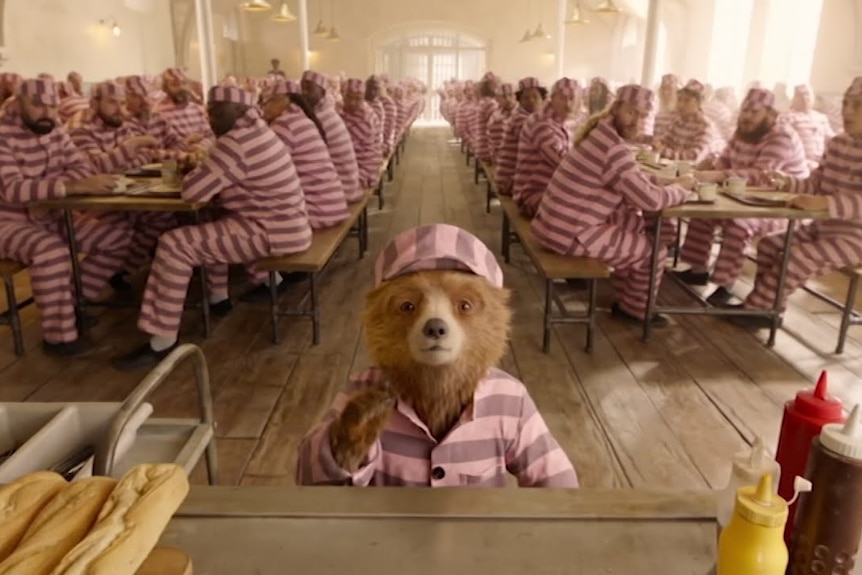 Paddington in a jail mess hall wearing striped clothes.