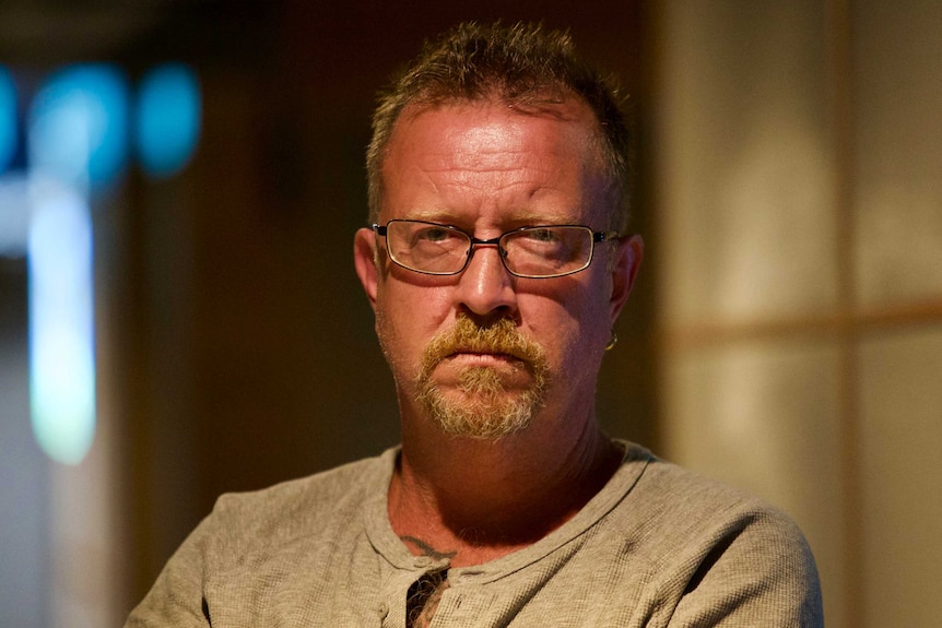 Andrew Hodson, wearing glasses and an earring, stares down the barrel of the camera intensely.