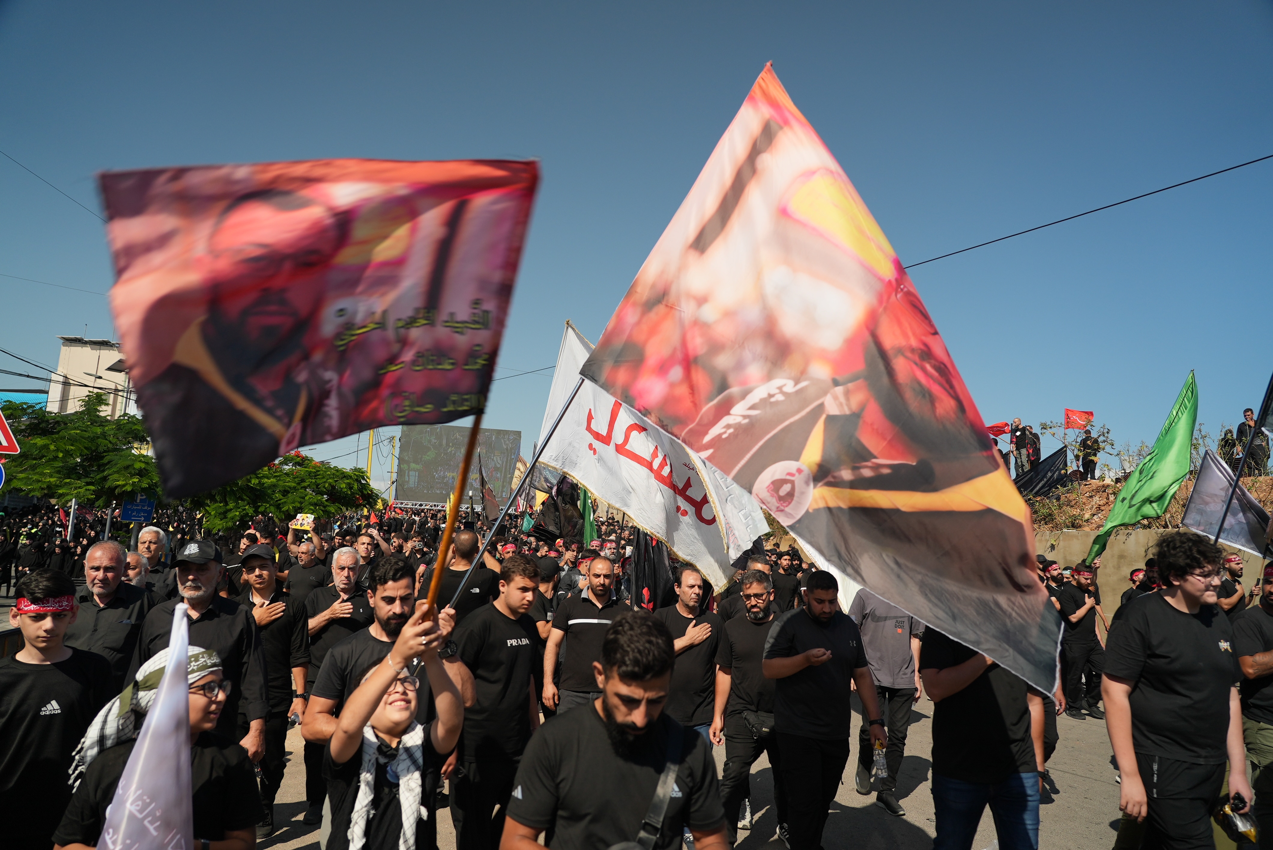 Men dressed in black holding up large flags of men killed fighting for Hezbollah.
