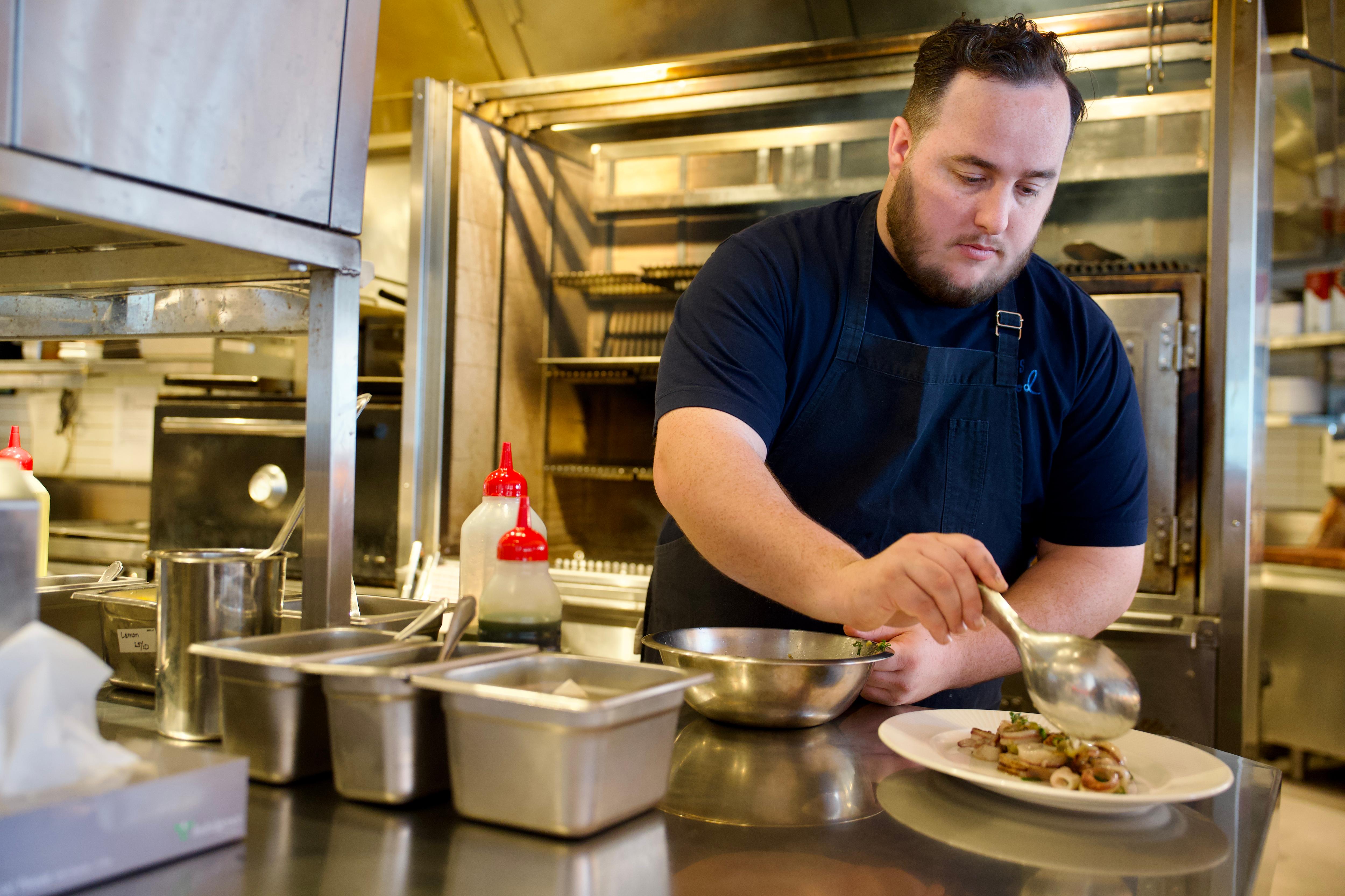 Head chef Luke Bourke working on serving his signature calamari dish, ladling freshly cooked seafood onto a white plate