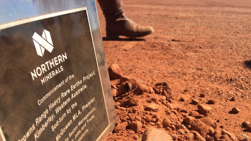 A sign explaining a new mine sits in red dirt as a person walks past in boots