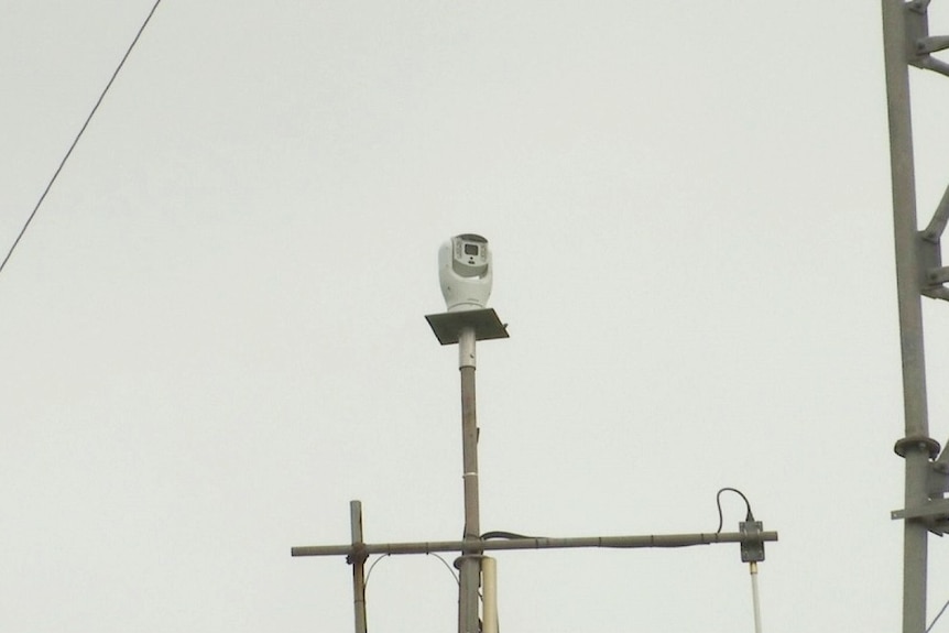 Close-up shot of a small white camera sitting on top of a metal tower.