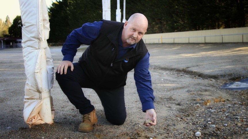 Crouching man picks up a rock on a sports oval.