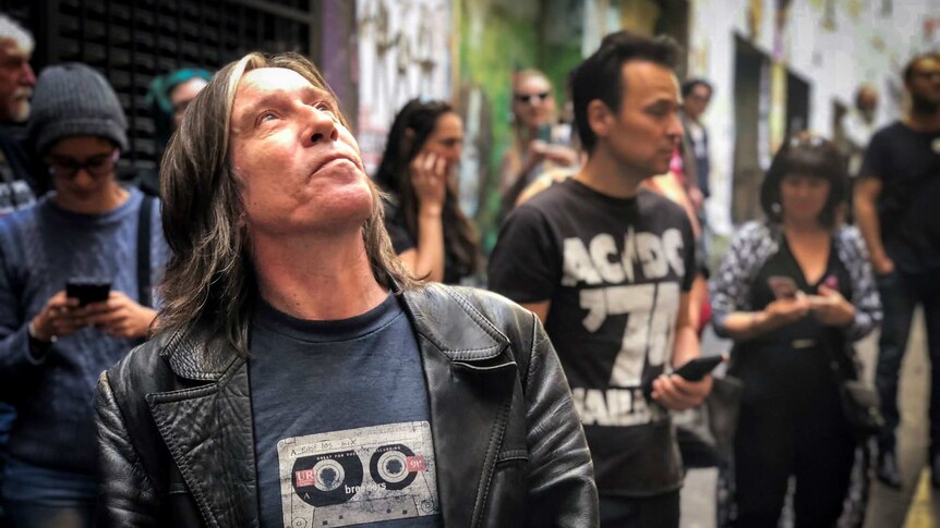 A man looks up at an artwork of Bon Scott in Melbourne's AC/DC lane.