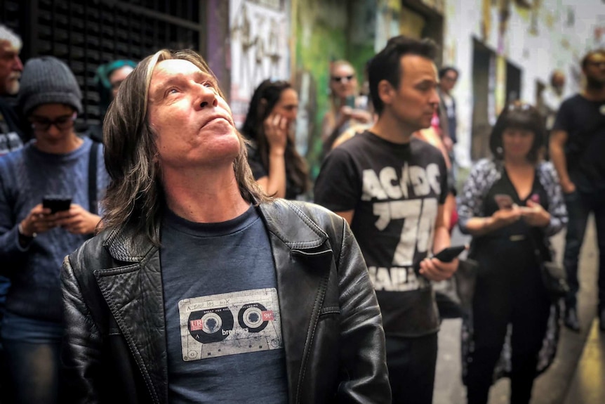 A man looks up at an artwork of Bon Scott in Melbourne's AC/DC lane.