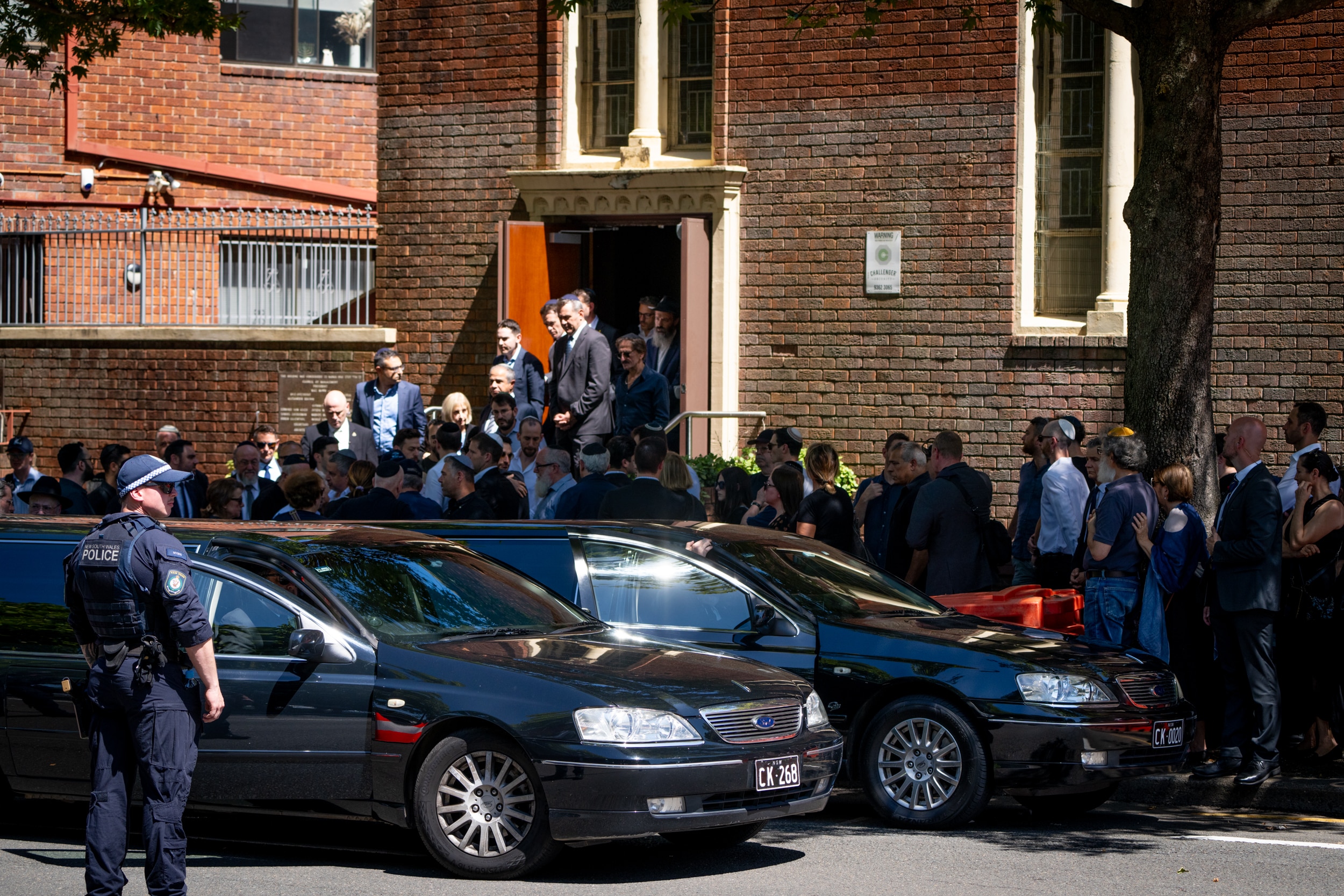 Un grupo de personas se reúne frente a una funeraria mientras un oficial de policía permanece cerca.
