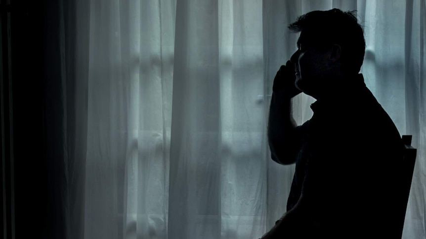 Darrin Todd, holding phone sitting on chair, silhouetted against a curtain background
