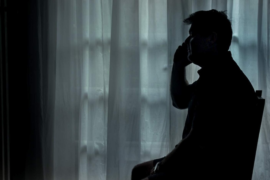 Darrin Todd, holding phone sitting on chair, silhouetted against a curtain background