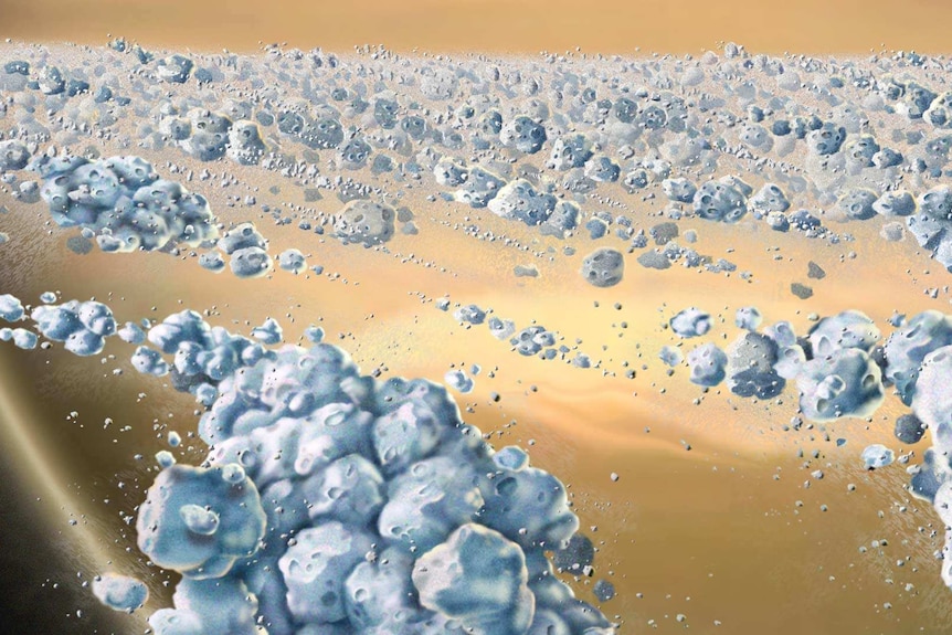 An illustration of thousands of large and small chunks of ice are floating together around a large yellowy-orange planet