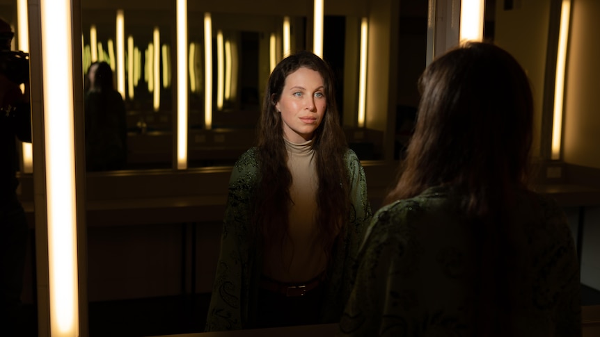 A woman looks in the mirror at a stage