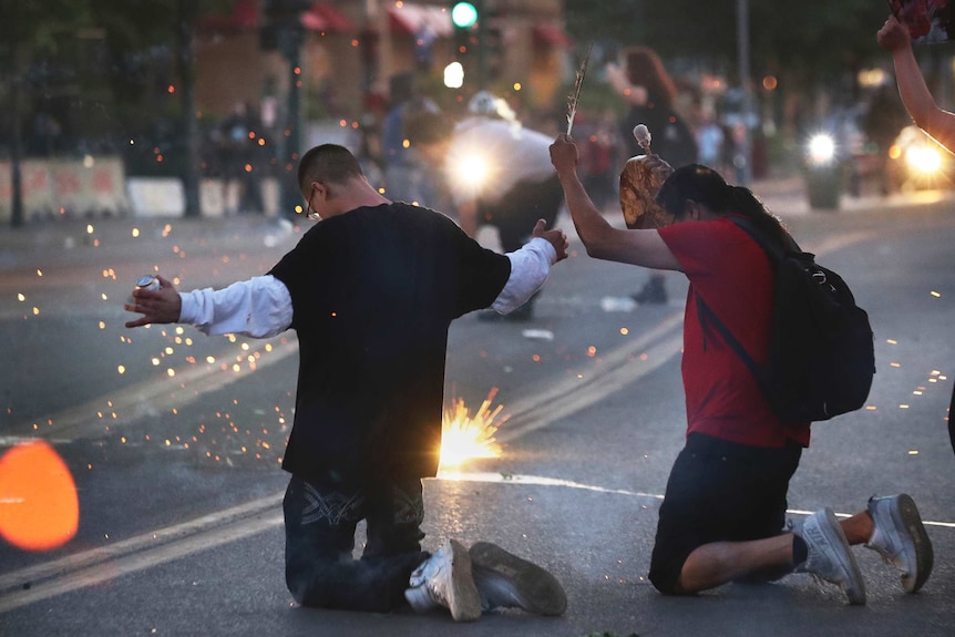 Two men kneeling down while concussion grenades explode before them