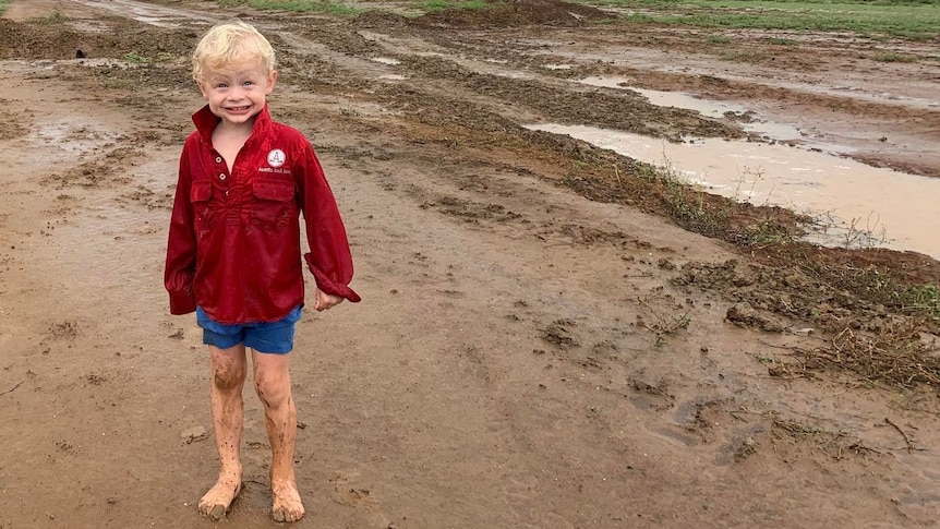 A young boy stands barefoot in muddy rain