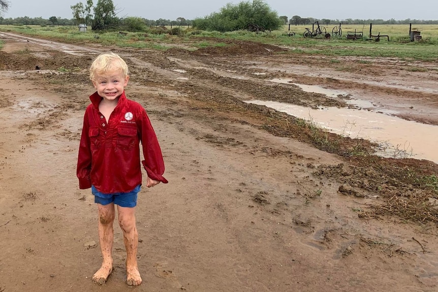 A young boy stands barefoot in muddy rain