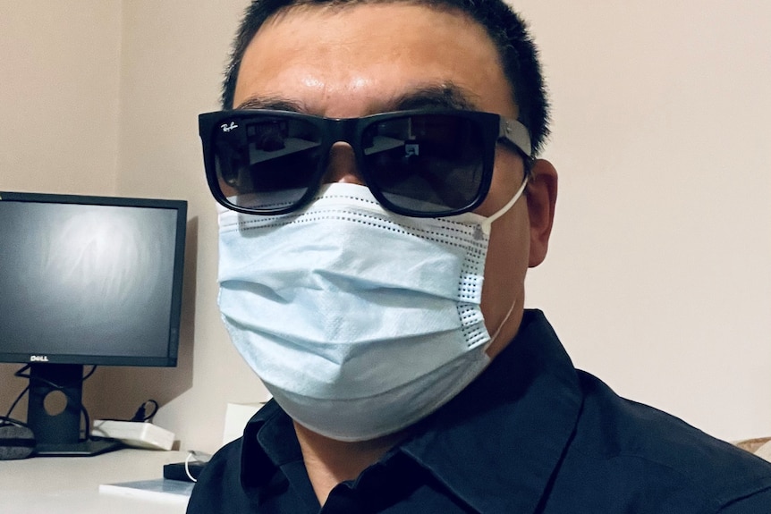 a man with face mask and a pair of sunglasses sitting in front of a computer desk