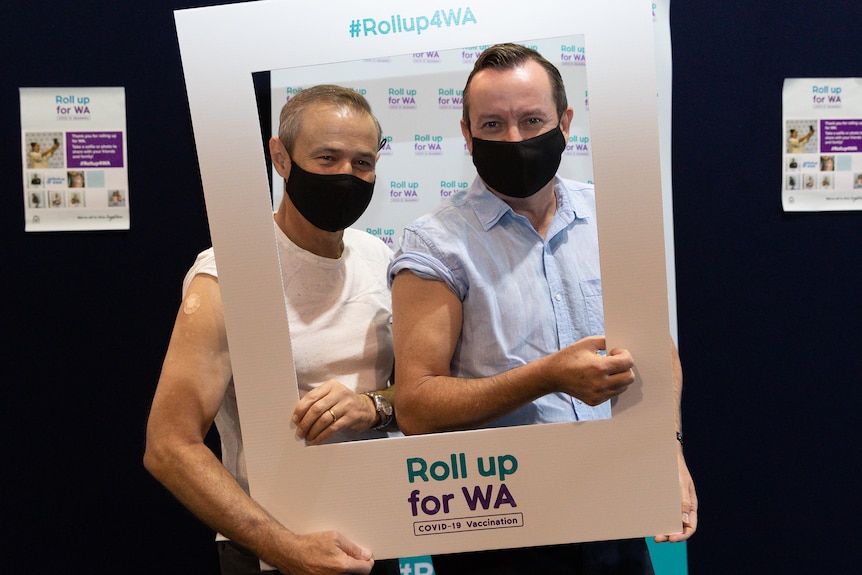 Two men pose for a photo with their arms exposed after receiving a vaccination