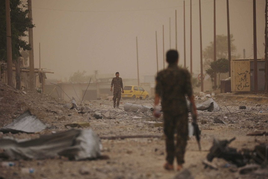 Two soldiers walk towards each other from opposite ends of a debris-covered street