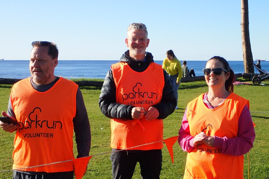 Erno van Alphen is pictured with two other parkrun volunteers in orange high-visibility vests 