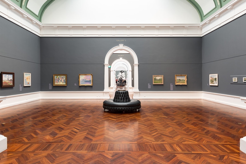 19th century gallery with parquetry flooring, dark grey walls, a black leather banquette, Impressionist paintings on walls.