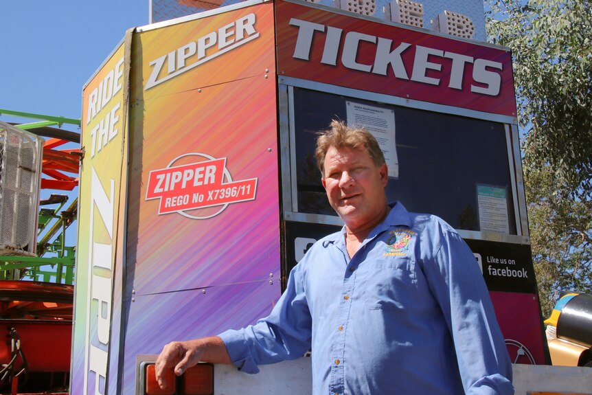 A man stands in front of a carnival ride ticket booth 