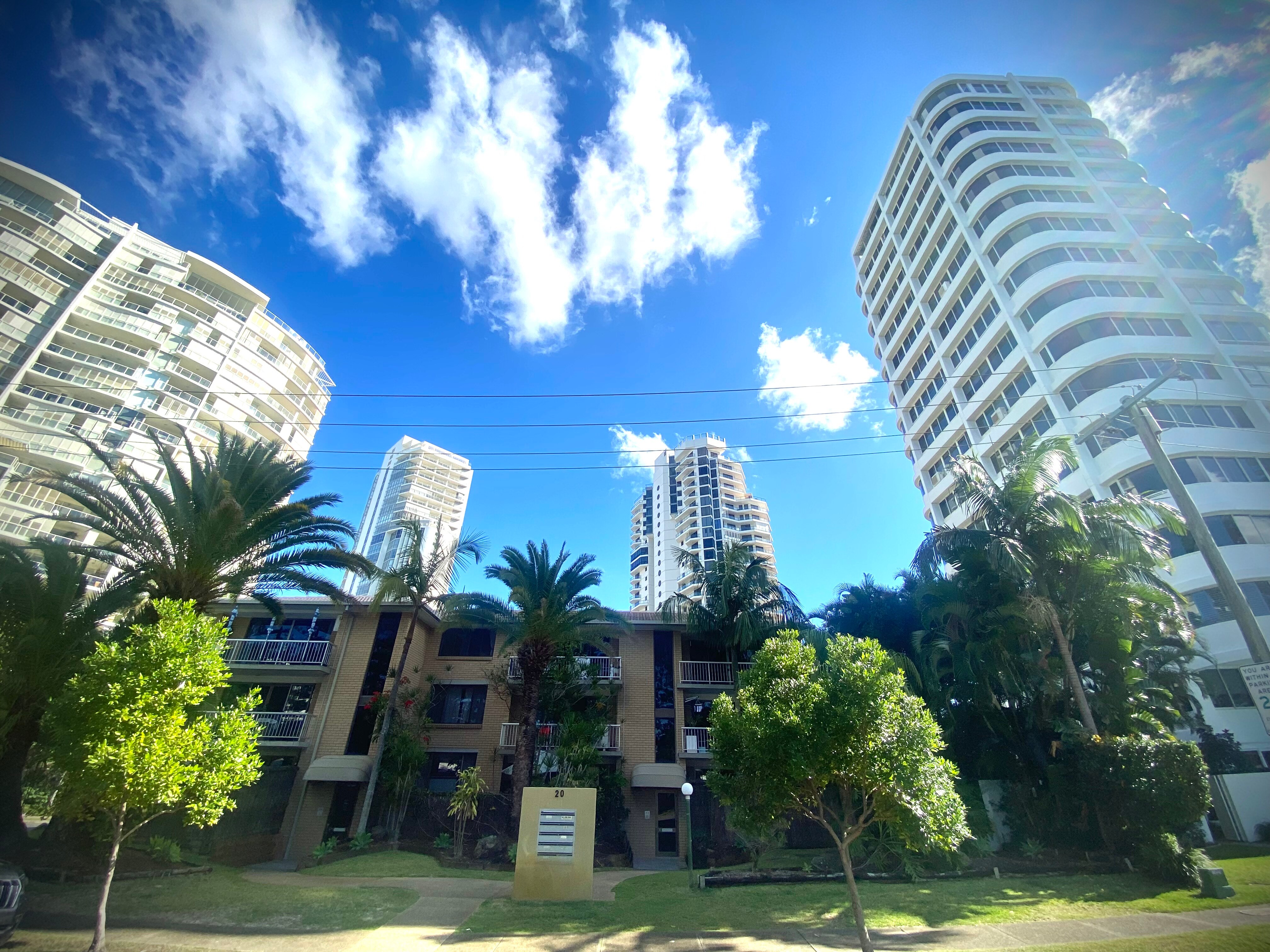 A small, three-storey unit complex built in red brick is surrounded by large white high-rise apartment towers.