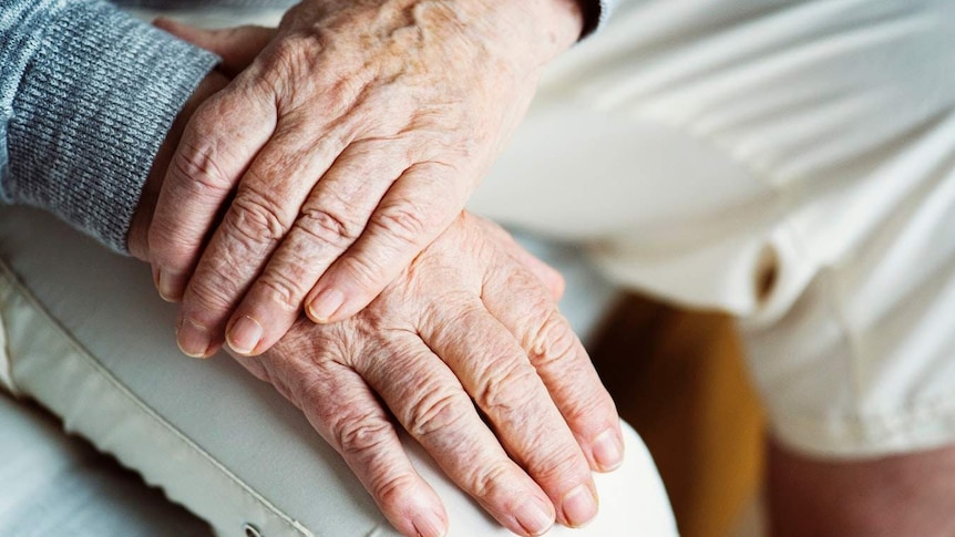 An elderly man crosses his hands.