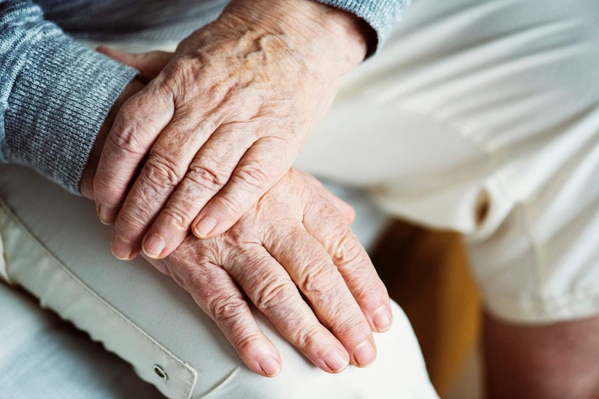 An elderly man crosses his hands.