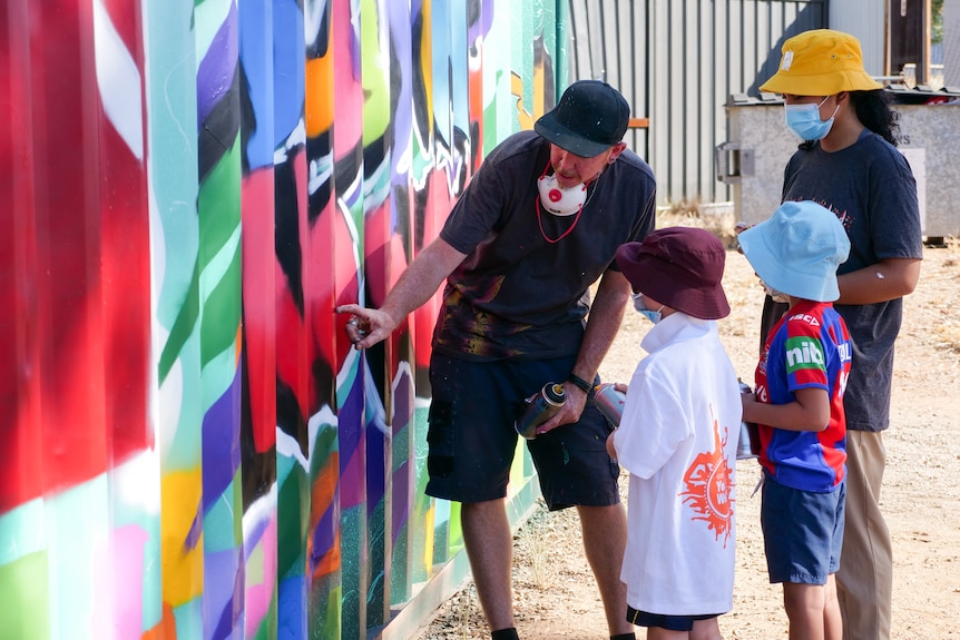 Three children stand next to a man pointing at a graffiti piece.